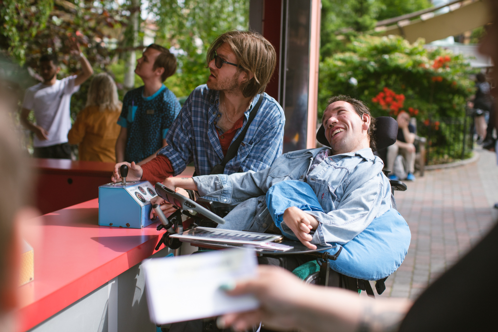 En kille i rullstol, som får hjälp av sin assistent, att köra spelet Milkshake på Liseberg.