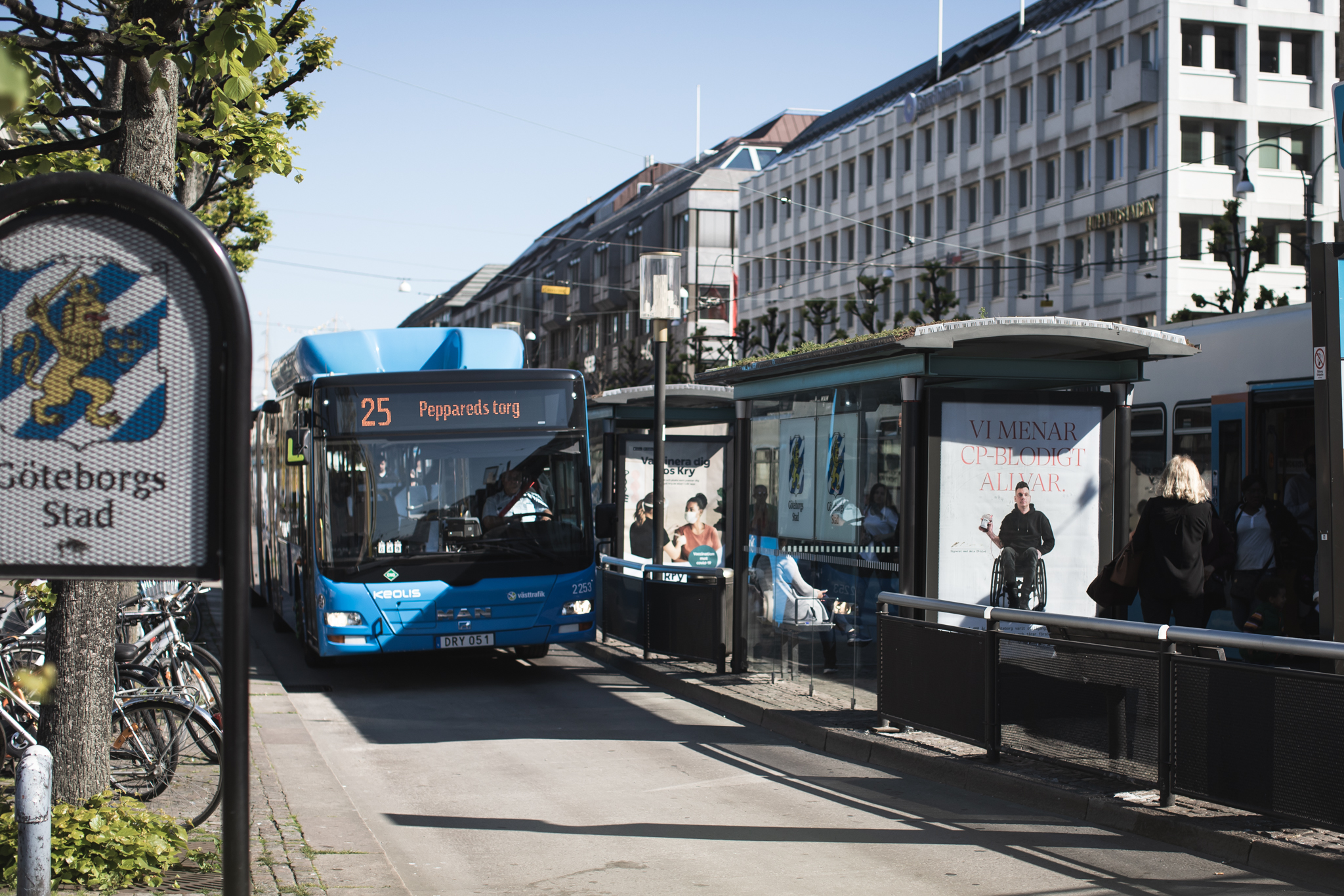 Stadsmiljö med bussar, hus och skyltar, på reklamplatsen sitter en poster från kampanjen CP-blodigt allvar. Anders håller i en blodpåse, text: Vi menar CP-blodigt allvar.