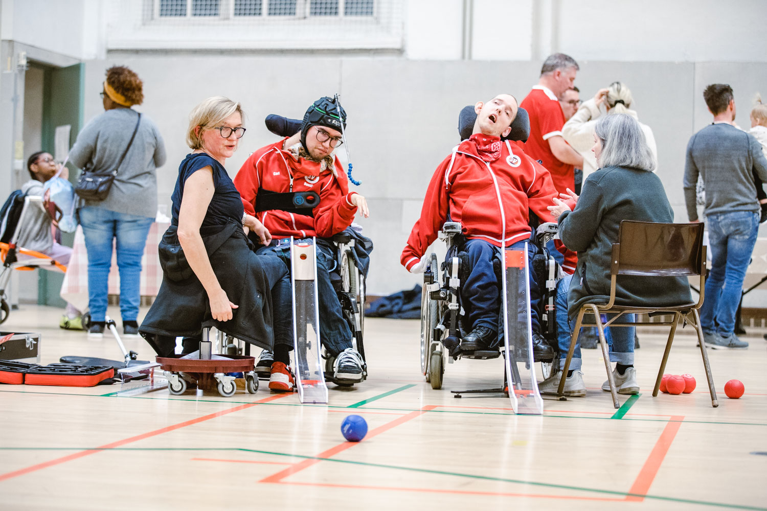 Carl och Einar spelar boccia, assistenterna sitter framför, den ena kollar ut mot plan.