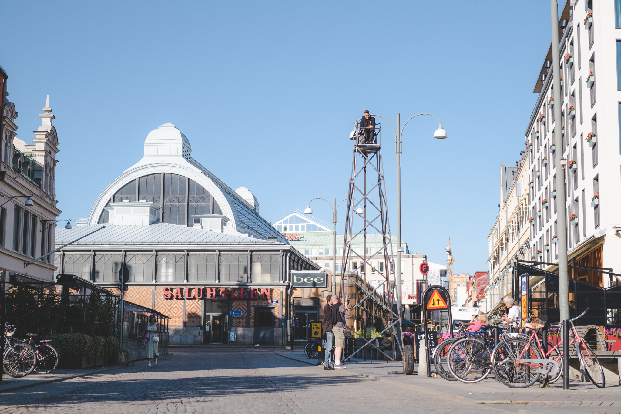 Stadsmiljö med saluhalli bakgrunden. I förgrunden ett torn av stål och en man längst upp.