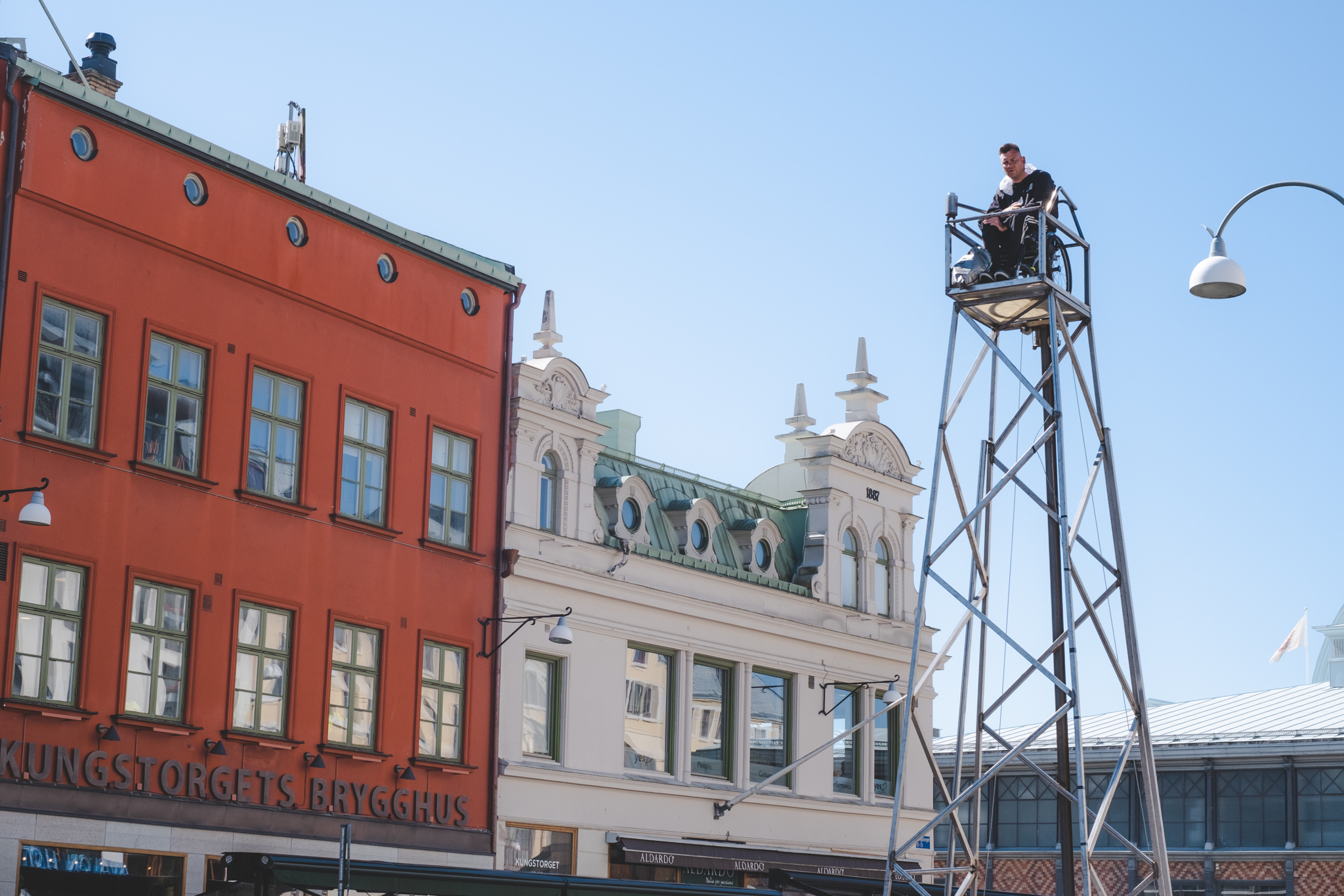 Fasader och ett torn, längst uppe sitter en man i rullstol.