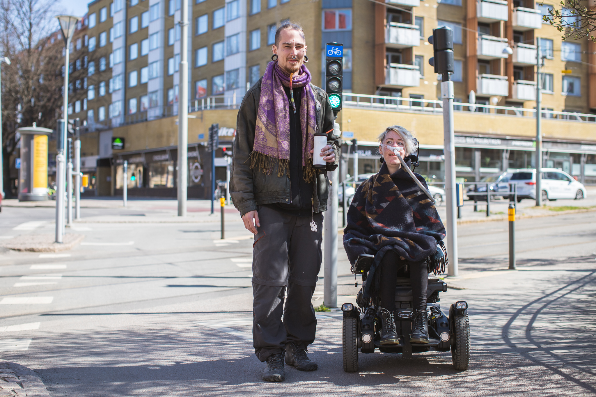 Tjej i elrullstol och hennes assistent går över gatan i stadsmiljö