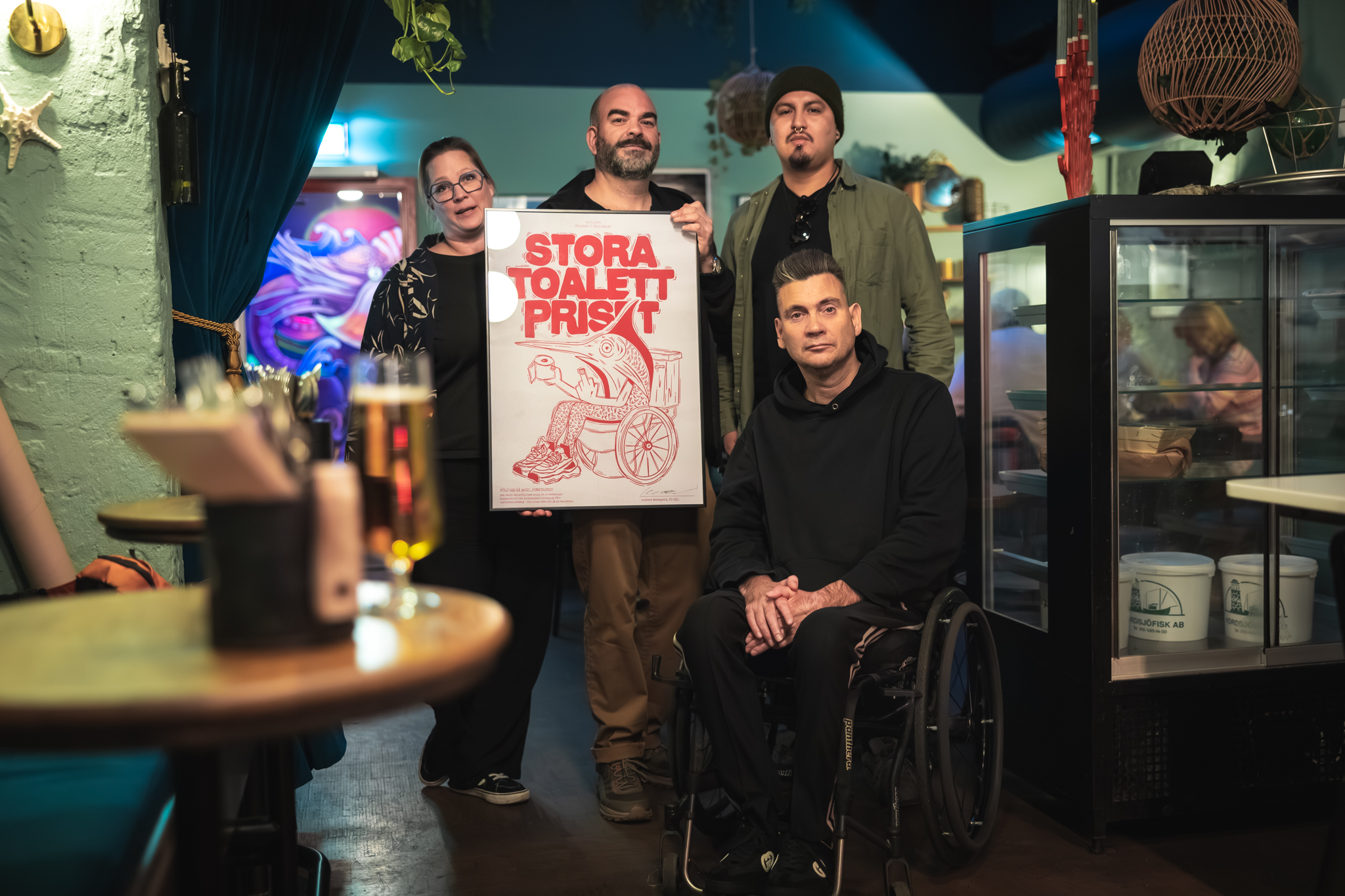 Personalen håller upp det inramade toalettpriset, som föreställer en fisk på toaletten