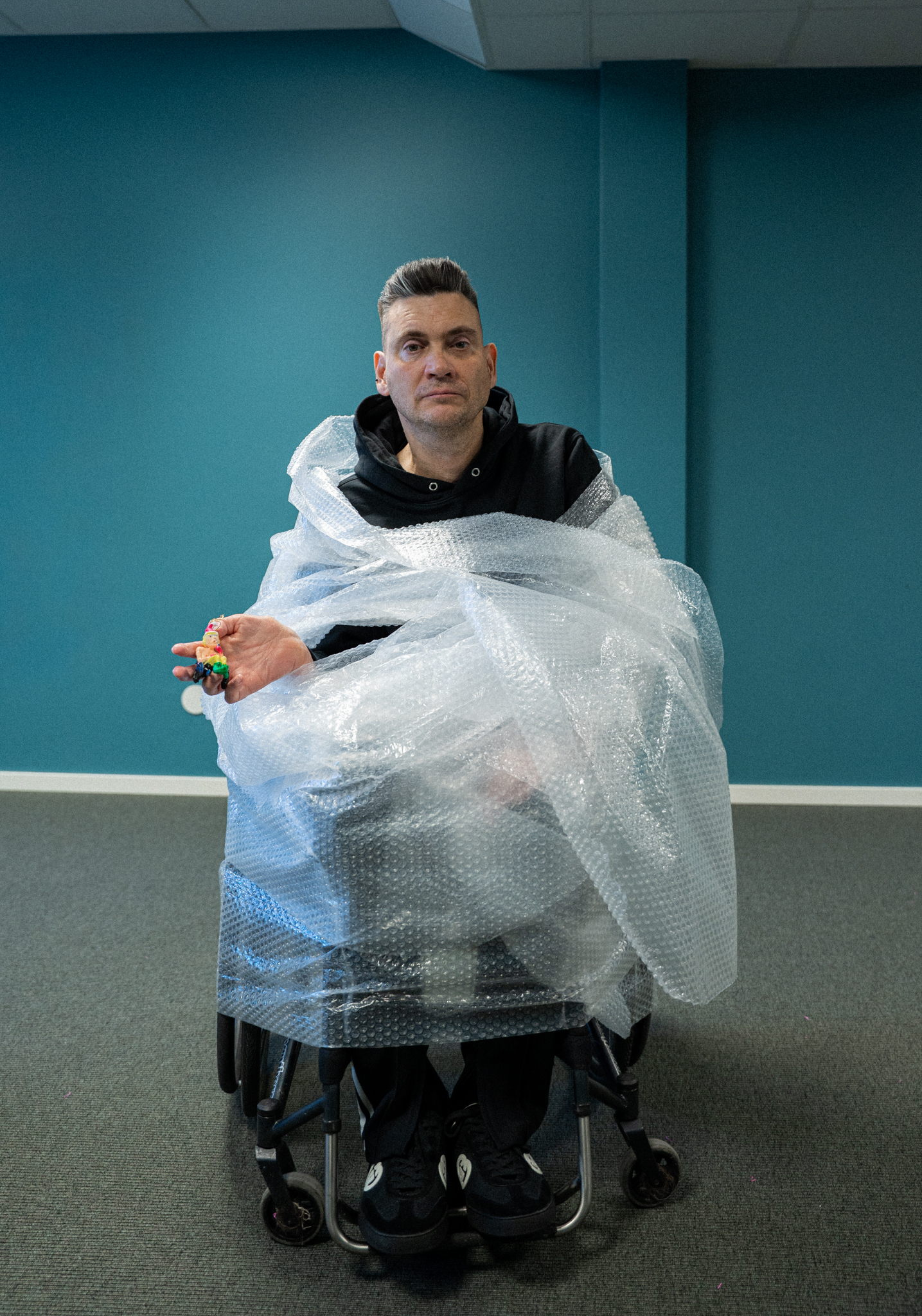 En  man, hans ansikte syns knappt, det är täckt av klisterdekaler med texten Hanteras varsamt och Hanteras ej varsamt. Julig omgivning.