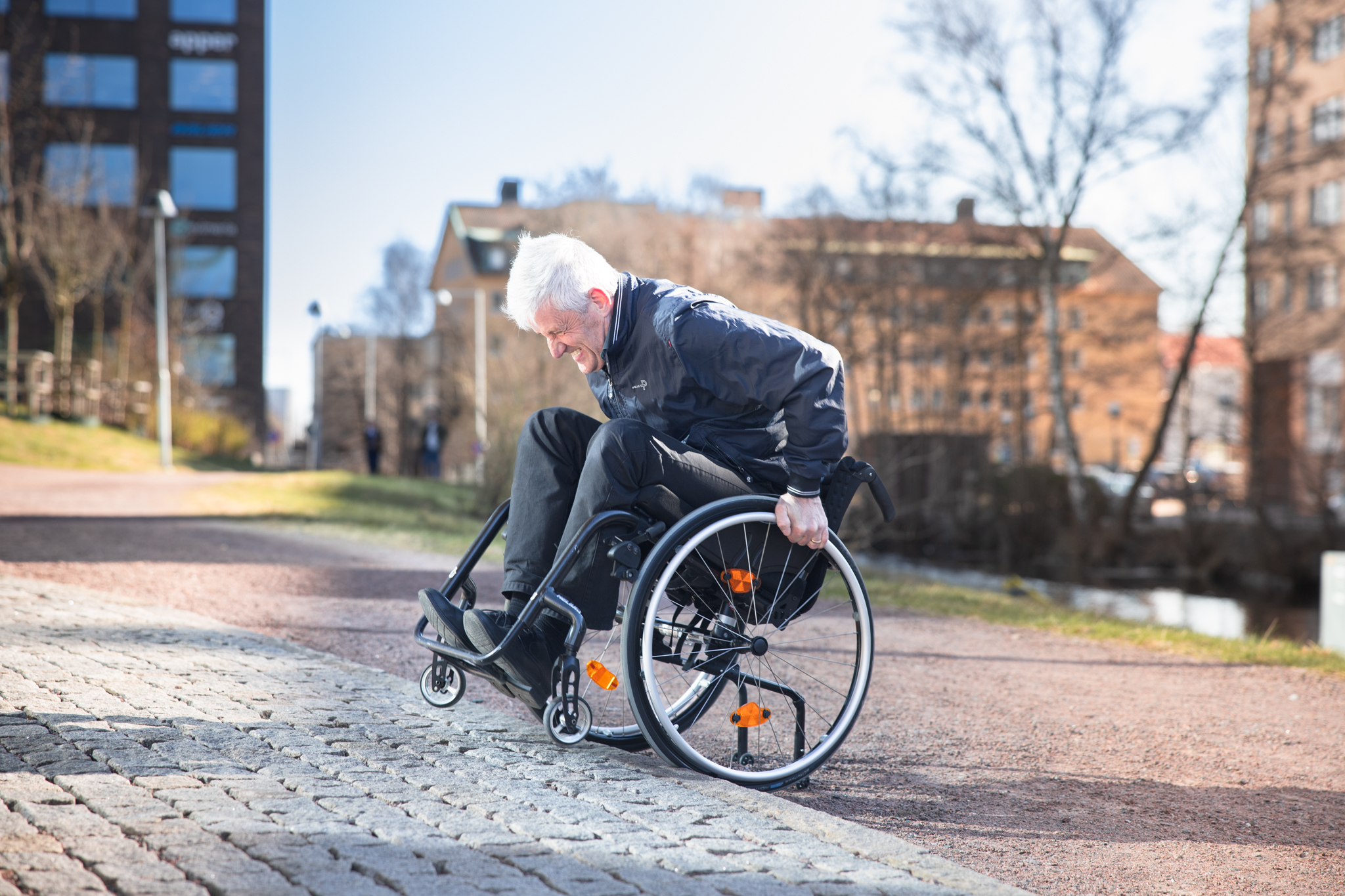 Man i rullstol tar i ordenligt för att komma upp för en kantsten, parkmiljö.
