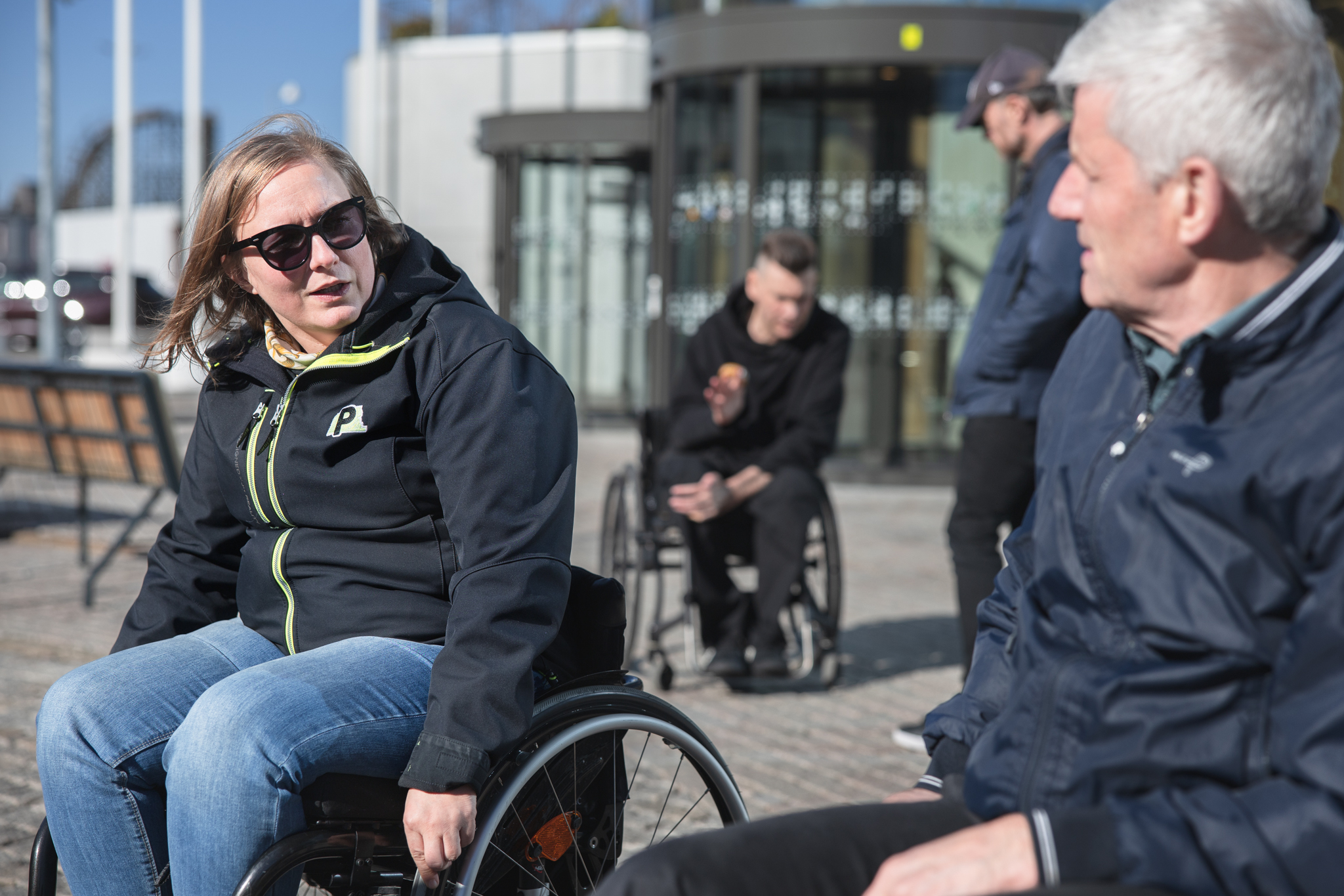 Flera personer i rullstol pratar i olika grupper, utomhusmiljö.